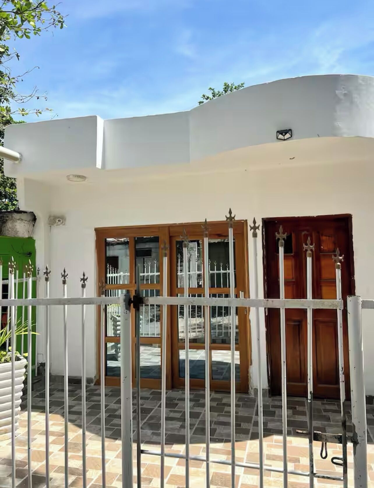 Un edificio con fachada blanca, una entrada porticada con puertas de madera y un patio con suelo de baldosas.