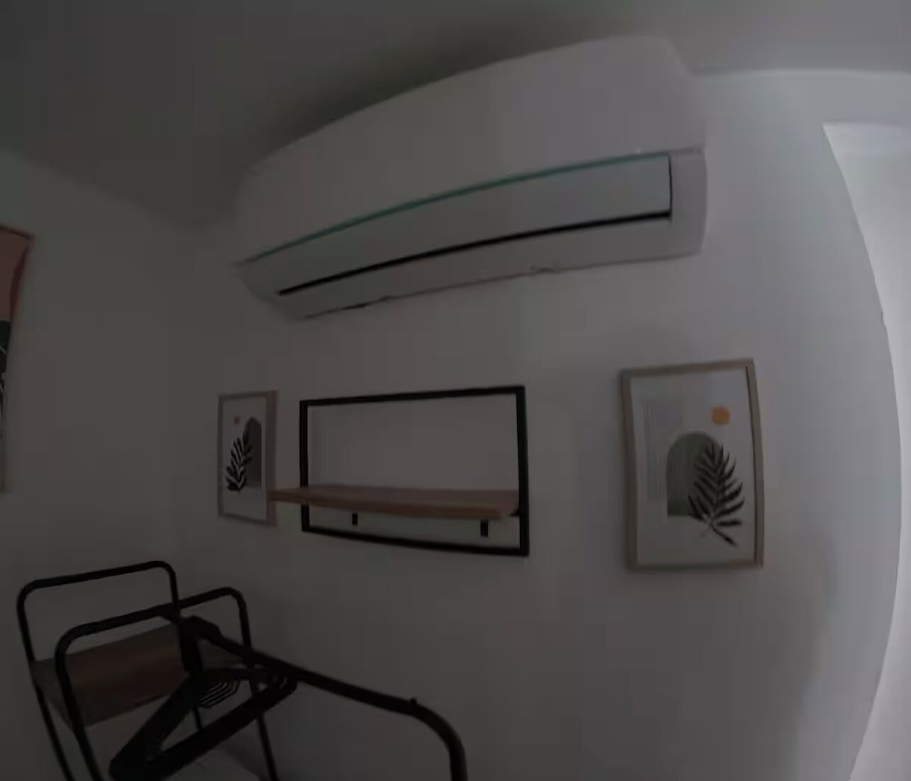 A room with a white wall, a black-framed chair, a glass shelf, and two framed leaf designs.