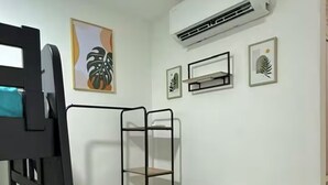 Une petite pièce comprenant un lit superposé, une commode blanche, un panier en osier et un appareil de climatisation fixé au mur.