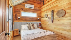 A wooden cabin bedroom with a bed, a window, and a wall-mounted air conditioner.