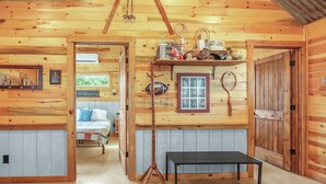 A wooden cabin interior with a bed, a table, and shelves with various items.