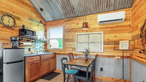 A wooden cabin interior with a kitchen, dining area, and a window.