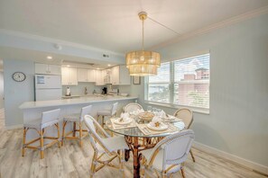 A modern kitchen with white cabinets, a central island, and a dining area with wicker chairs and a glass table. - Vacation Villas #531 Cute Beachfront Corner Condo (Fort Myers Beach)