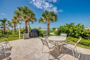 An outdoor patio with a round table and chairs, surrounded by palm trees and greenery.