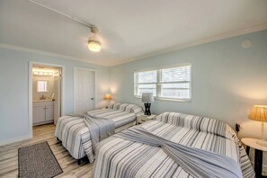 A bedroom with two beds, a nightstand, a lamp, a window, and a bathroom visible through an open door.