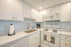 A kitchen with white cabinets, a stainless steel sink, a microwave, a stove, and a coffee maker.
