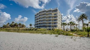 Un hotel de varios pisos con balcones, situado cerca de una playa de arena con palmeras.