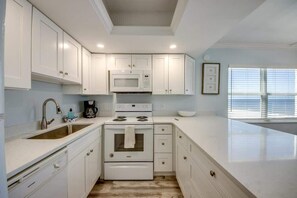 A modern kitchen with white cabinets, a microwave, stove, and sink.