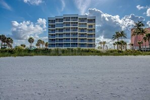 A multi-story hotel with a modern design, located on a beach with palm trees and a clear sky.