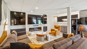 A modern living room with a sofa set, a fireplace, and a kitchen area in the background.