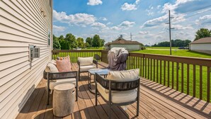 A wooden deck with outdoor furniture, including chairs and a table, overlooking a green lawn and a residential area.