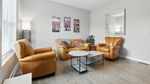 A living room with a sofa, two armchairs, a coffee table, and a cityscape painting on the wall. - Cozy Historic Row Home- Near Stadiums! 3 Bedroom Home (Pittsburgh)