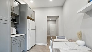 A modern kitchen with grey cabinets, a white refrigerator, and a microwave. There is a dining area with a table and chairs, and a white vase with pampas grass on the table. - Cozy Historic Row Home- Near Stadiums! 3 Bedroom Home (Pittsburgh)