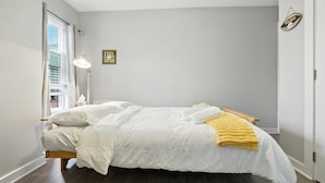 Ein Schlafzimmer mit einem Bett, einer Nachttischlampe, einem Fenster mit Vorhängen, einer Wanduhr und einer Tür.