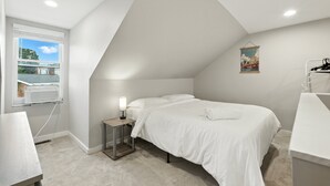 A bedroom with a bed, a bedside table with a lamp, a window with blinds, and a poster on the wall. - Cozy Historic Row Home- Near Stadiums! 3 Bedroom Home (Pittsburgh)