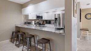 Una cocina moderna con armarios blancos, electrodomésticos de acero inoxidable, una encimera de granito y tres taburetes de bar.