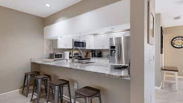 A modern kitchen with white cabinets, stainless steel appliances, a granite countertop, and three bar stools.