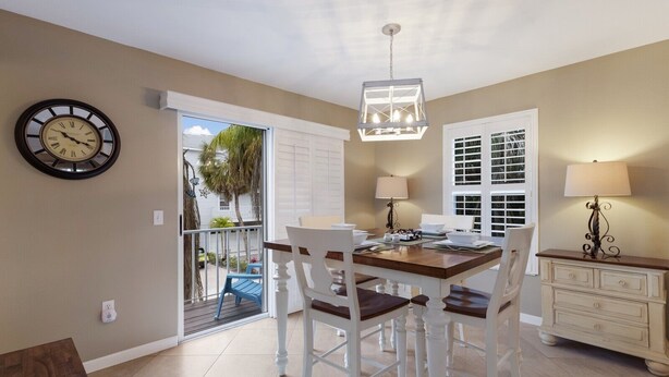 A dining area with a wooden table, white chairs, a chandelier, and a clock on the wall. - North Beach Village #62 3 Bedroom Home (Holmes Beach)