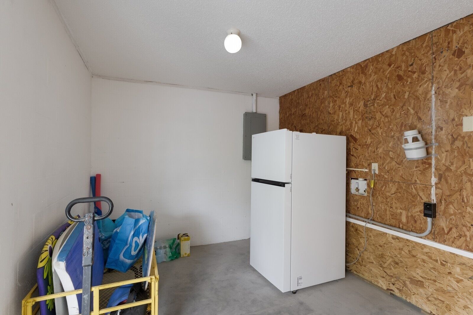 A small, enclosed room with a white refrigerator, a wooden wall, and a metal rack with cleaning supplies.