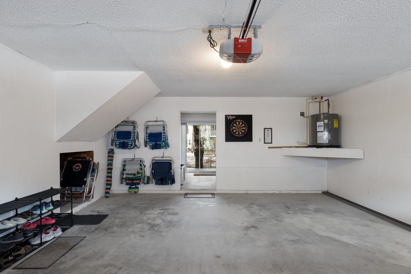 En rummelig garage med betongulv, loftmonteret projektor, dartskive og vandvarmer.
