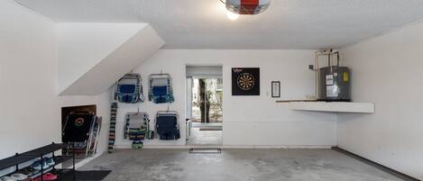 En rummelig garage med betongulv, loftmonteret projektor, dartskive og vandvarmer.