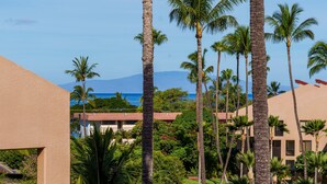 A resort with palm trees, a view of the ocean, and a mountain in the background. - Kamaole Sands #5-401 2 Bedroom Condo (Kihei)