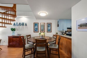 Ein Essbereich mit Holztisch und -stühlen, eine Küche mit hellblauen Schränken sowie eine Treppe mit Holzgeländern.