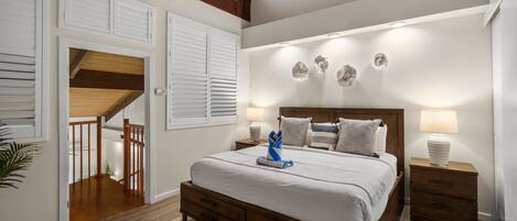 A bedroom with a wooden bed, a ceiling fan, a staircase, and a view of the outdoors.