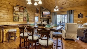 Interior rústico de una cabaña con comedor de madera, chimenea y televisor.