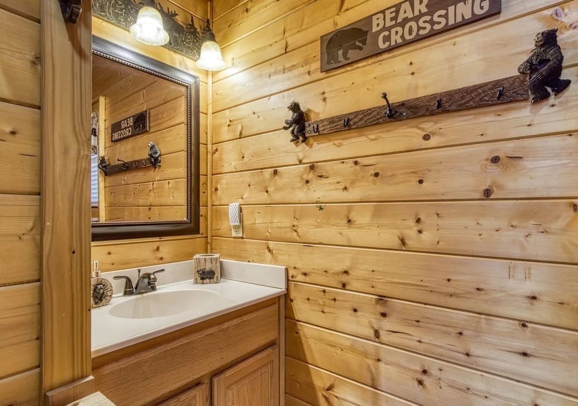 Une salle de bain rustique, aménagée dans une cabane en bois, avec un grand miroir, un lavabo et un panneau d’avertissement indiquant un passage fréquent d’ours.
