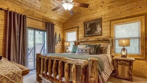Un dormitorio rústico de madera con una cama grande, un ventilador de techo y una ventana con persianas.