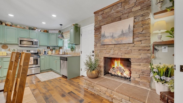 Une cuisine moderne avec des meubles de couleur verte, une cheminée en pierre et un coin repas avec des chaises en bois.