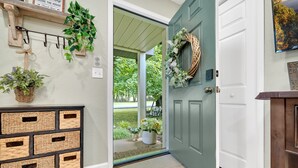 Une porte en bois avec une sonnette verte et une guirlande, un panier tressé accroché au mur et un paillasson devant l’entrée.