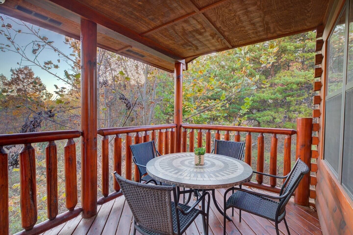 A wooden deck with a round table and chairs, surrounded by a wooden railing.