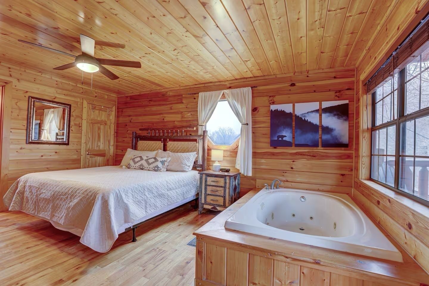 Une chambre dans une cabane en bois, comprenant un lit, une table de chevet, une lampe, une fenêtre et une grande baie vitrée ornée d’œuvres d’art.