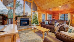 A cozy cabin interior with a fireplace, leather sofa, wooden coffee table, and large windows. - All Ya Need 4 Bedroom Cabin (Sevierville)