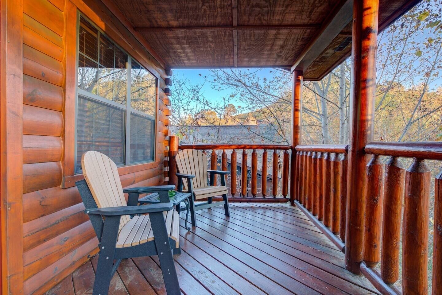 Eine Holzhütte mit Veranda, ausgestattet mit zwei Adirondack-Stühlen und einem kleinen Tisch.