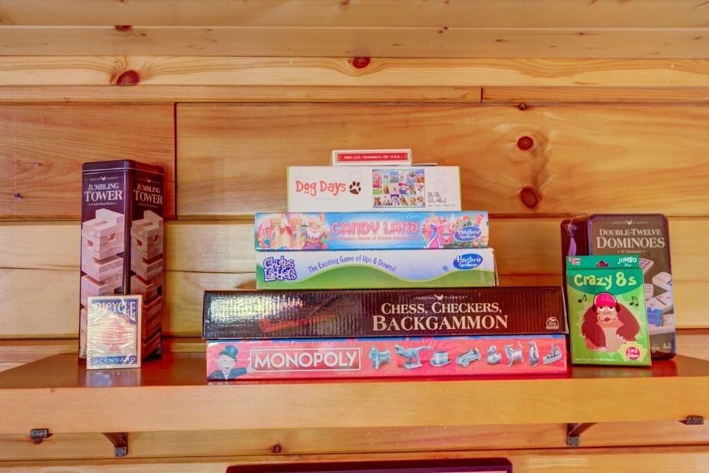 A wooden shelf with various board games including JUMBO TOWER, DOG DAYS, CANDY LAND, DOUBLE-TWELVE DOMINOS, CHESS, CHECKERS, BACKGAMMON, MONOPOLY, and CRAZY 8S.
