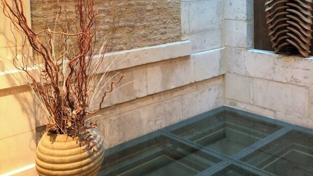 A stone wall with a window and a glass table in the foreground. - Studio Mezzanine place du marché (La Rochelle)