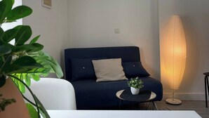 A modern living room with a dark blue sofa, a white coffee table, and a tall floor lamp. - Studio Mezzanine place du marché (La Rochelle)