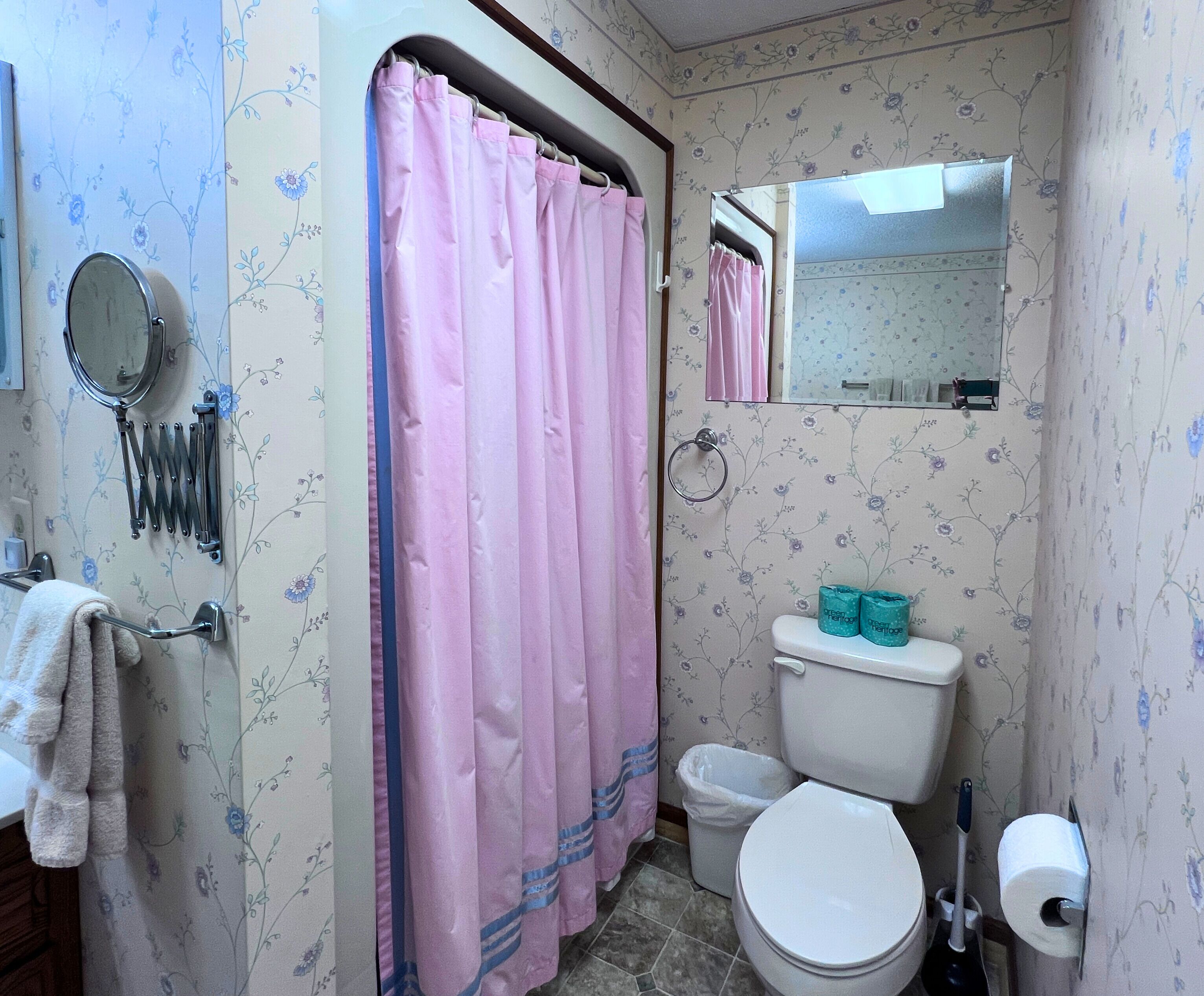 A bathroom with a pink shower curtain, a toilet, a bidet, a mirror, and a towel rack.