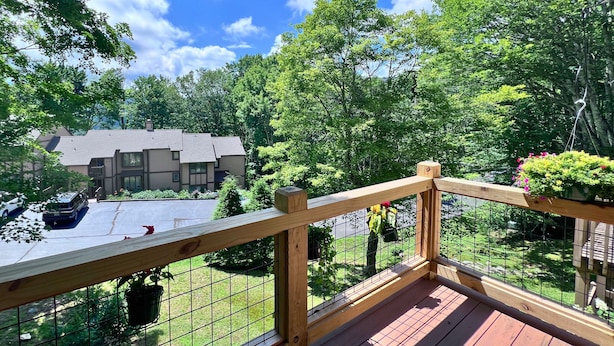 A wooden deck with a metal railing overlooking a parking area and a building with a grey roof. - Charming two-bedroom, two-bathroom condo minutes away from Sugar Mnt. Resort (Sugar Mountain)
