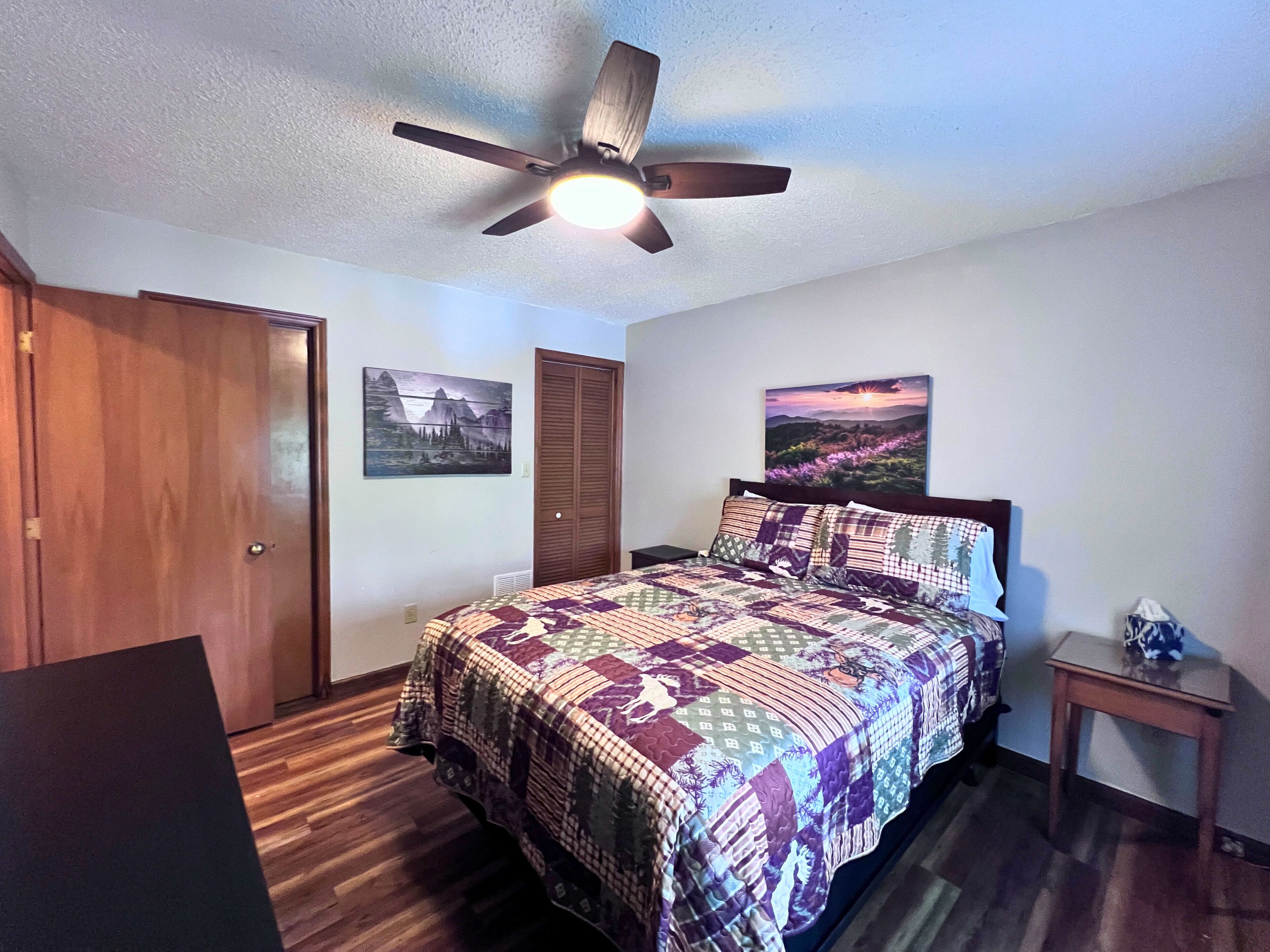 A bedroom with a bed, a ceiling fan, two doors, and two wall-mounted paintings.