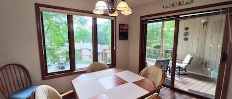 A dining area with a wooden table and chairs, large windows, and a view of the outdoors.