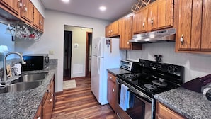 A kitchen with wooden cabinets, a stainless steel sink, a microwave, a refrigerator, a stove, and a toaster. - Charming two-bedroom, two-bathroom condo minutes away from Sugar Mnt. Resort (Sugar Mountain)