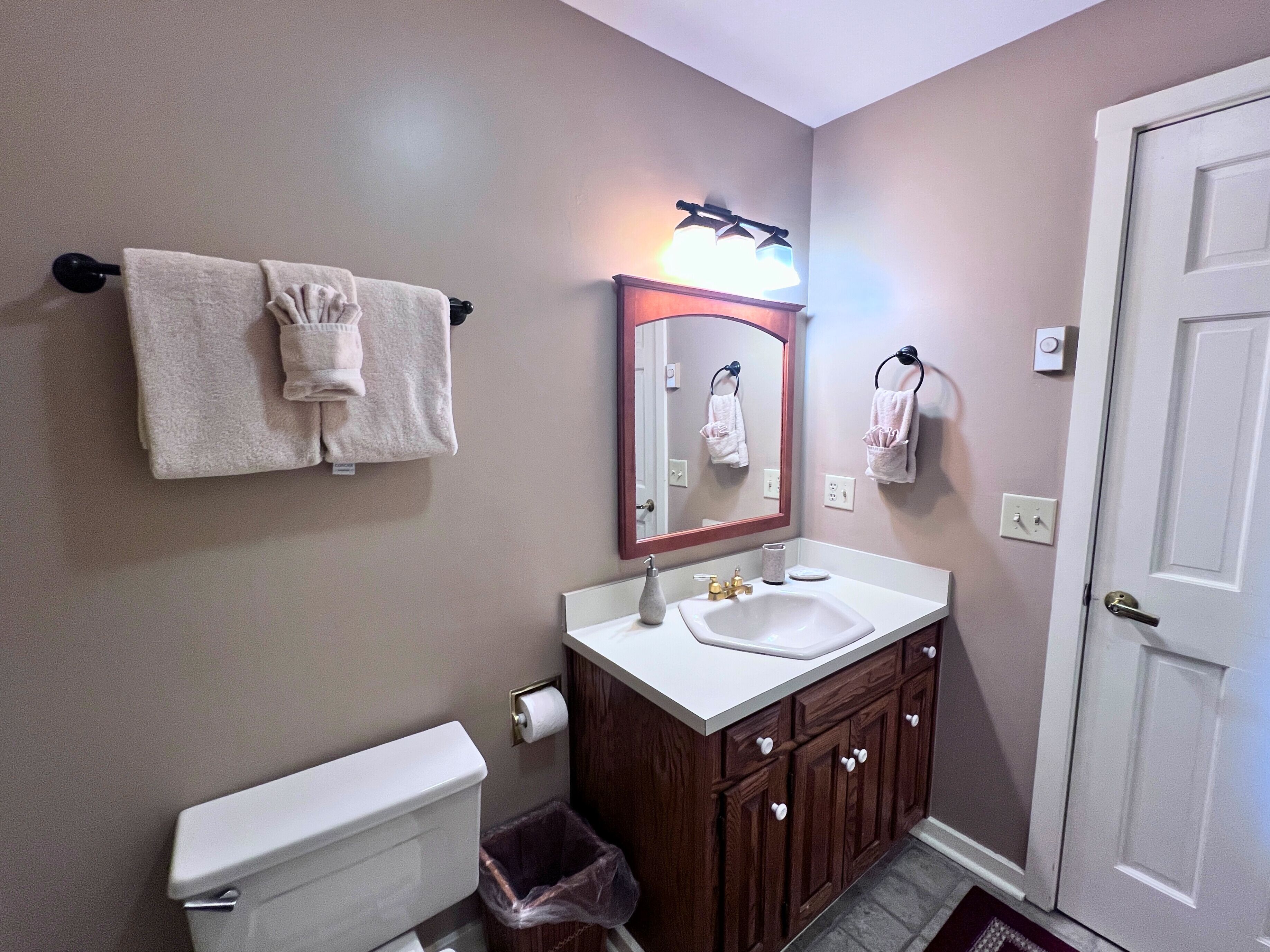 A bathroom with a toilet, sink, mirror, and towel rack.