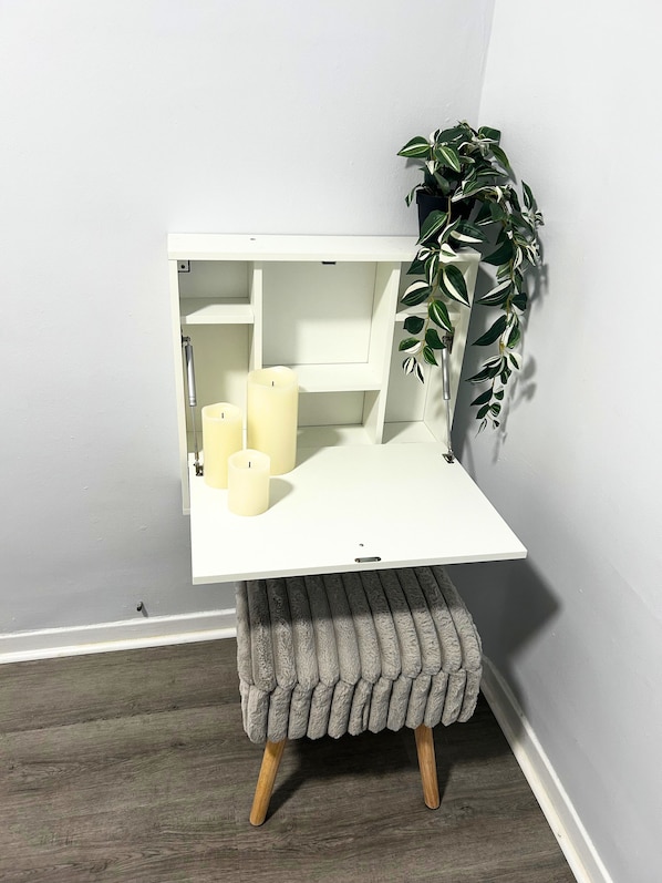 A corner vanity with a white countertop, three candles, and a potted plant.