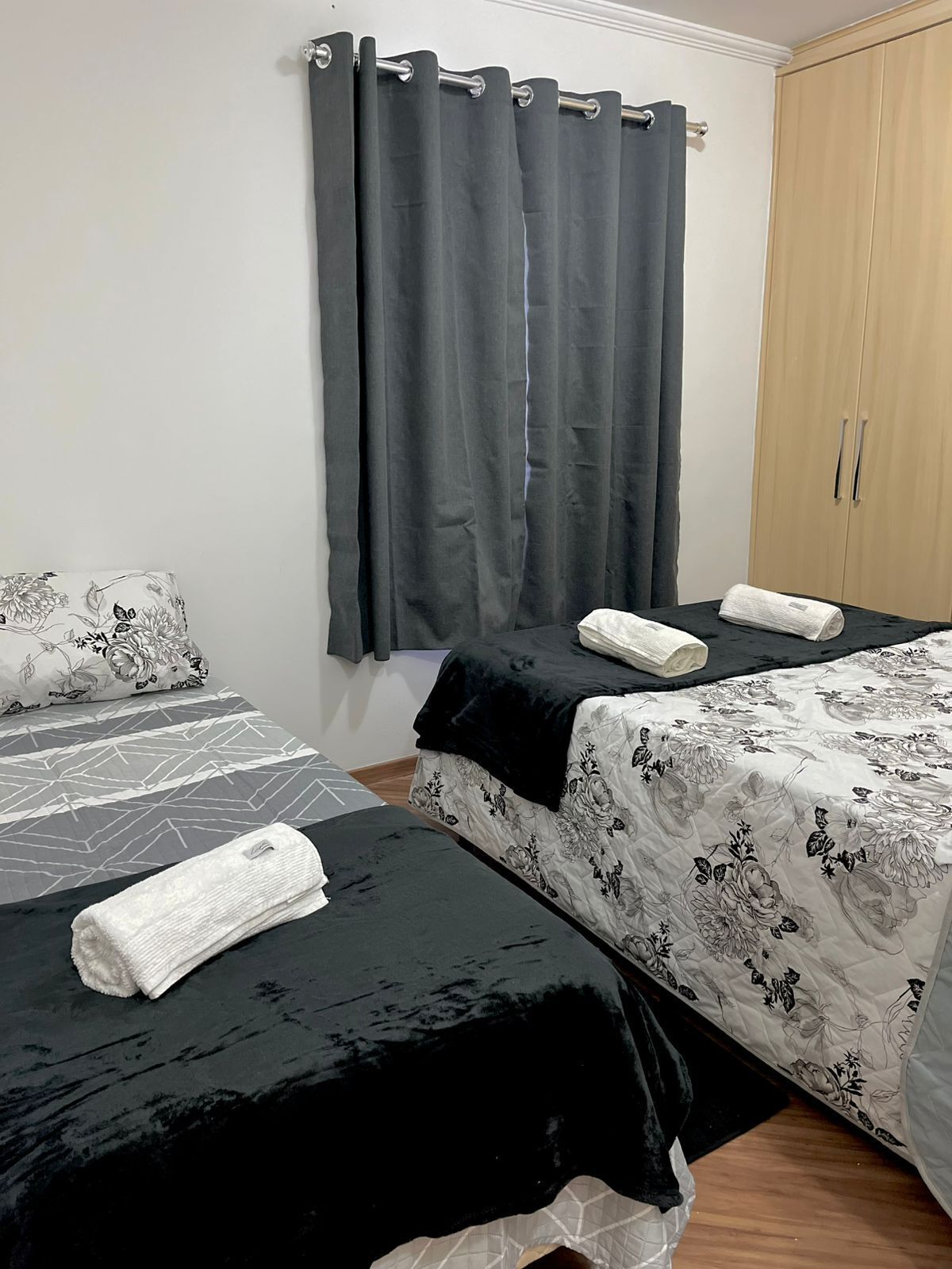 Habitación con dos camas, cada una con una colcha floreada en blanco y negro, y una cortina gris.
