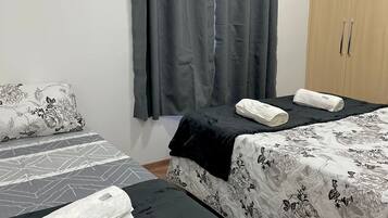 Habitación con dos camas, cada una con una colcha floreada en blanco y negro, y una cortina gris.