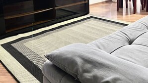 A modern living room with a flat-screen TV on a dark wooden TV stand, a potted plant, a dining area with a wooden table and chairs, and a grey sofa. - Apartment in front of Colinas shopping mall (Jardim das Colinas São José dos Campos)